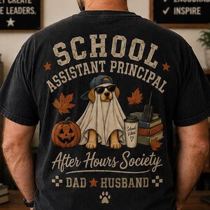 May include: A black short-sleeve t-shirt featuring a graphic of a dog wearing a ghost costume, sunglasses, and a baseball cap. The design includes a pumpkin, books, and the text School Assistant Principal After Hours Society Dad Husband.