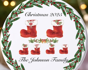 May include: A white Christmas ornament with a festive design. It features red Christmas stockings with names, surrounded by a green and red wreath. The text "Christmas 2025" and "The Johnson Family" are also displayed.