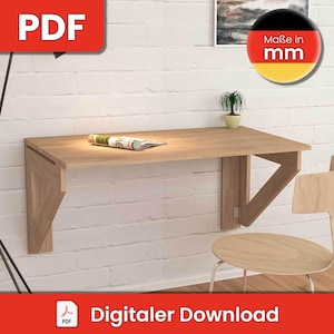 Puede incluir: Un escritorio de pared plegable de madera con una revista encima. El escritorio está fijado a una pared de ladrillo blanco. Una silla de madera está en primer plano. El texto "Maße in mm" es visible en la esquina superior derecha de la imagen.