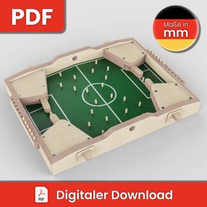 Könnte beinhalten: Ein hölzernes Tischspiel mit einer grünen Filzspielfläche in Form eines Fußballfeldes. Das Spiel hat Holzstücke und einen Holzrahmen. Das Spiel ist mit "Maße in mm" beschriftet, was "Maße in Millimetern" bedeutet.