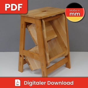 May include: A wooden step stool with a natural finish. The stool is folded up and has a step on each side. The stool is made of solid wood and has a simple design. The stool is labeled "Maße in mm" which means "Measurements in millimeters".