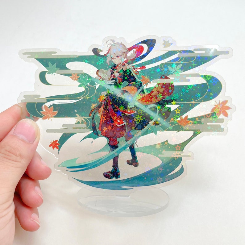 May include: A clear acrylic standee featuring a character illustration with a holographic effect. The character is depicted in a detailed outfit with a flowing cape, set against a backdrop of stylized clouds and maple leaves. The standee is held by a hand.