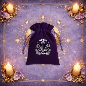 May include: A deep purple velvet drawstring pouch featuring a white screen-printed graphic of three crystals, a crescent moon, and leafy sprigs. The bag is centred, with a gathered top and matching purple cord ties for closure.