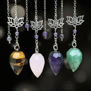Puede incluir: Cuatro péndulos de piedras preciosas facetadas que cuelgan de cadenas plateadas. Cada uno presenta un dije de loto plateado con un símbolo Om, pequeñas cuentas moradas y una piedra en forma de lágrima de ojo de tigre, cuarzo rosa, amatista y aventurina verde.