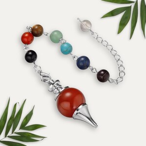Könnte beinhalten: Ein Pendel mit roter, abgerundeter Basis und silberfarbener Spitze. Die Kette ist mit einer Reihe farbiger Edelsteinperlen verbunden, darunter rot, braun, grün, blau und schwarz. Am Ende der Kette befindet sich eine transparente Kristallperle.
