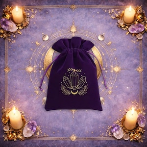 May include: A deep purple velvet drawstring pouch featuring a gold-coloured graphic print of three crystals, a crescent moon, and leafy branches. The pouch is centred, with four white pillar candles placed at the corners of the frame.