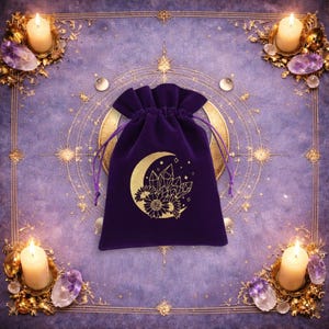 May include: A deep purple velvet drawstring pouch featuring a gold-coloured graphic print of a crescent moon, crystals, and sunflowers. The pouch has matching purple fabric cords for closure and is centred on a purple surface with gold accents.