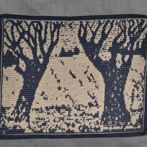 May include: A rectangular, crocheted wall hanging depicting a forest scene. The design uses a cream-coloured background with navy blue trees and a dark blue border. The trees have detailed branches against a light-coloured background.