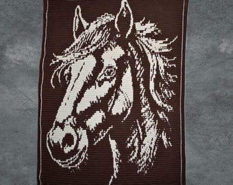 May include: A brown and white crochet blanket with a horse's head design. The horse's head is depicted in white against a brown backdrop, with a white border. The blanket showcases a detailed equine portrait.