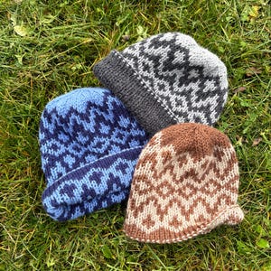 Peut inclure: Trois bonnets en tricot avec un motif géométrique répétitif. Un bonnet est bleu et bleu foncé, un autre est gris et gris foncé, et le troisième est marron et beige. Chaque bonnet possède un revers plié et une texture en laine épaisse.
