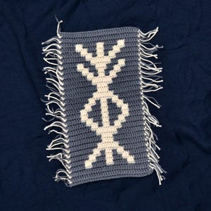 May include: A gray crocheted rectangular pillow with a white geometric design. The pillow has white fringe on all sides.