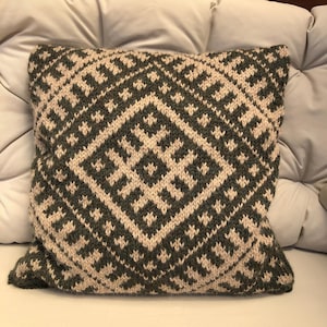 Peut inclure: Un coussin carré en tricot présentant un motif géométrique bicolore gris anthracite foncé et crème. Le design se compose d'un grand losange central formé de petits motifs répétitifs complexes, entouré d'une bordure aux motifs similaires.