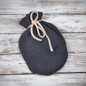 Puede incluir: Una bolsa de cordón de punto gris con un cordón blanco. La bolsa está sobre una superficie de madera blanqueada.