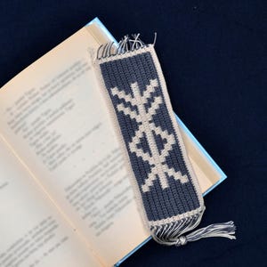 May include: A gray and white crocheted bookmark with a geometric pattern and a fringe tassel.