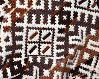 Puede incluir: Primer plano de una manta de crochet marrón, blanca y naranja con un patrón geométrico.