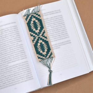 May include: A crocheted bookmark with a green and white geometric pattern and a tassel. The bookmark is on a white book.