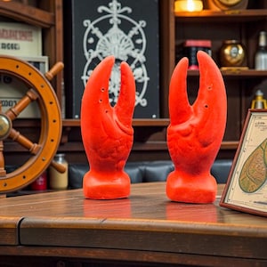 Peut inclure: Deux sculptures de pinces de homard rouge vif sont posées sur une table en bois. Les pinces sont détaillées et se tiennent debout. Un thème nautique est suggéré par le gouvernail et la carte en arrière-plan. Le cadre est un bar ou un restaurant.