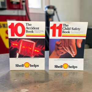 May include: Two white booklets titled The Accident Book and The Child Safety Book, numbered 10 and 11 in large red font. Each cover features the Shell logo and the text Shell helps. The first shows a red emergency light, the second shows hands.