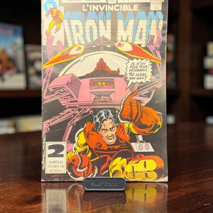 May include: A vintage L'Invincible Iron Man comic book featuring a double format cover with French text. The cover art displays a character in a red and yellow suit, a futuristic vehicle, and the text JE N'EN PEUX PLUS! DÉSORMAIS TU SERAS IRON MAN!