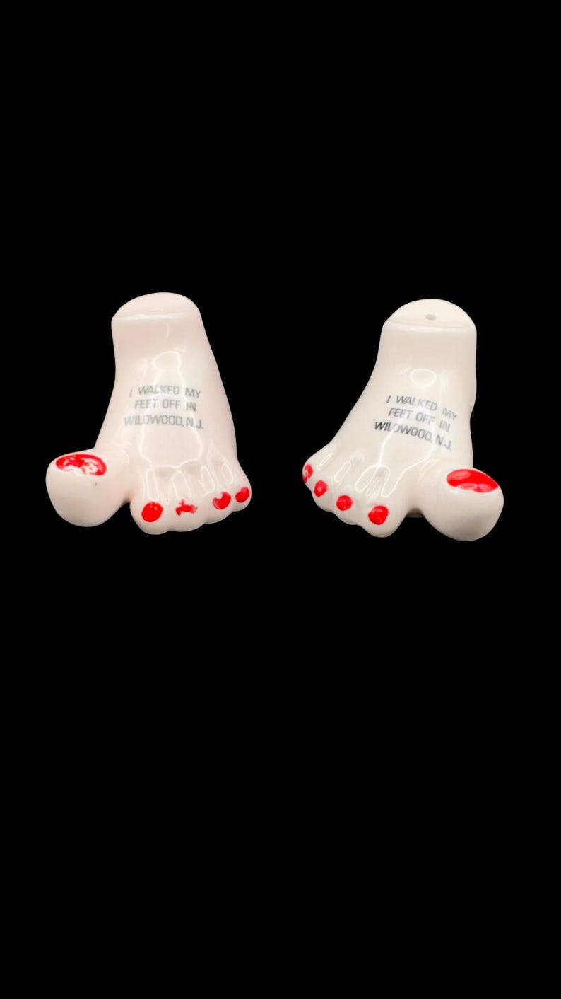 May include: A pair of ceramic salt and pepper shakers shaped like human feet with red painted toenails. Each foot features the black printed text I WALKED MY FEET OFF IN WILDWOOD, N.J. on the top surface, with small holes for dispensing seasoning.