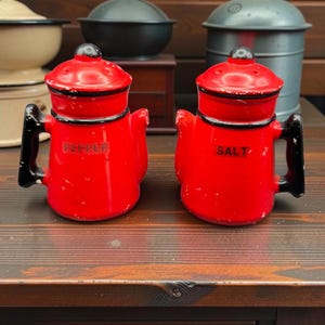 Peut inclure: Deux salières et poivrières en céramique rouge vif en forme de cafetières miniatures. Chaque pièce présente une anse noire, un couvercle noir avec un petit bouton et des bordures noires. Le mot PEPPER est inscrit sur l'une et SALT sur l'autre.