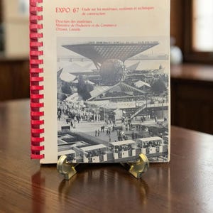 May include: A spiral-bound report titled EXPO 67 Etude sur les matériaux, systèmes et techniques de construction, Direction des matériaux, Ministère de l'Industrie et du Commerce, Ottawa, Canada, featuring a black and white photograph of the Expo 67 site.