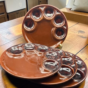 Peut inclure: Un ensemble de trois assiettes rondes en céramique brun brillant, chacune présentant six alvéoles circulaires disposées sur le bord extérieur. Les assiettes ont une finition lisse et réfléchissante d'une couleur brun foncé uniforme.