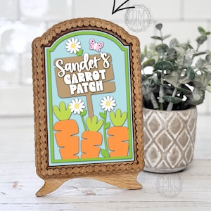 May include: Wooden sign with a decorative frame, featuring the text "Sander's Carrot Patch" and illustrations of carrots and daisies. The sign is on a wooden stand. The text "DIGITAL DOWNLOAD" is on the left side.