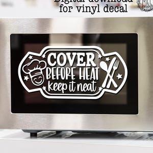 Könnte beinhalten: Ein Mikrowellenherd aus Edelstahl mit einer schwarzen Tür. Ein weißes Vinyl-Abziehbild auf der Tür lautet "COVER BEFORE HEAT keep it neat" mit Kochmützen-, Löffel- und Gabelgrafiken. Die Mikrowelle hat eine Digitalanzeige und Bedientasten.