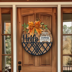 May include: A round wooden door wreath with a blue and black geometric design. The wreath features a white truck with the word "Pumpkin" on the side, and the words "Hello" in black script. The wreath is decorated with a large orange bow and fall foliage.