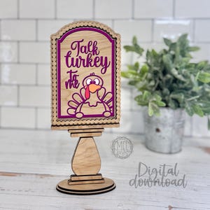 Może przedstawiać: Drewniany znak na Święto Dziękczynienia z ilustracją indyka i napisem "Talk turkey to me". Znak znajduje się w dekoracyjnej ramie i jest zamontowany na drewnianym stojaku. Znak jest do pobrania cyfrowo.
