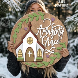 May include: A round wooden sign with the words "Amazing Grace" in white script. The sign features a church illustration with a cross, surrounded by green leaves and purple hearts. The words "DIGITAL DOWNLOAD" are in the upper right corner.