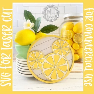 May include: A round wooden sign with a white background and a yellow lemon design in the shape of Mickey Mouse. The sign is surrounded by lemons and a jar of lemons.