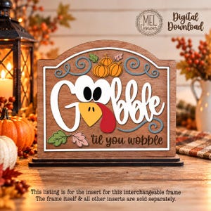 May include: A wooden sign insert featuring the text "Gobble 'til you wobble" with a turkey-themed design. The word "Gobble" is written in white with a turkey face, beak, and wattle. It includes orange pumpkins and colorful leaves.