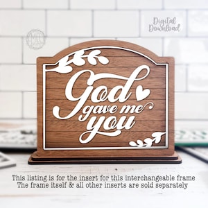 May include: A wooden sign with the words "God gave me you" in white script. The sign has a brown wood grain background and a white border. Decorative leaves are on the corners. The sign is for an interchangeable frame.