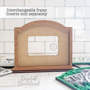 May include: A wooden interchangeable frame with a rectangular opening. The frame has a light brown finish with a darker brown base. The text "Interchangeable frame Inserts sold separately" is at the top. The words "Digital Download" are at the bottom.