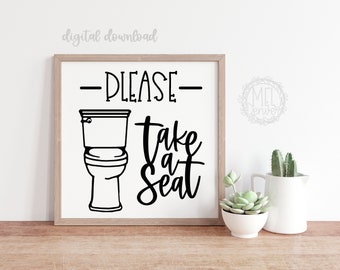 May include: A square framed wall sign featuring a black line drawing of a toilet and the black text PLEASE take a seat. The sign has a white background and a light wood frame. The text digital download is visible in the upper left corner.