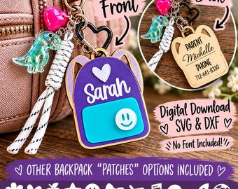 May include: A personalized backpack-shaped keychain featuring a purple base, a teal pocket, a white heart, and the name Sarah in white script. It includes a pink heart charm, a green dinosaur charm, and a white cord tassel on a black heart-shaped clasp.