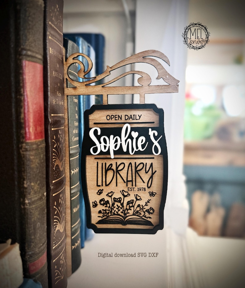 May include: Wooden sign for "Sophie's Library" with a decorative top, hanging in front of a bookshelf. The sign has a black border, with the words "Open Daily", "Sophie's", and "Library" in white. The sign also includes the text "EST. 1978".