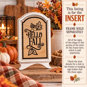 May include: A rectangular wooden sign insert with a light wood finish and a black arched border. The text "HELLO FALL" is printed in black, accompanied by black leaf illustrations at the top and bottom. The sign has a white scalloped frame.