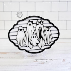 May include: A black and white decorative sign featuring a family of five ghosts. The ghosts are arranged in a horizontal line within a scalloped oval frame with horizontal slats. The text "MEL DENVER" appears in a small circular logo at the top left.