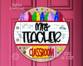 Puede incluir: Un letrero circular de madera con un diseño de papel rayado con el texto Mrs. TEACHER en negro y CLASSROOM en rojo. El borde superior muestra crayones y estrellas de colores, mientras que la parte inferior presenta un lápiz amarillo.
