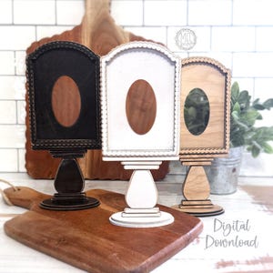 May include: Three wooden display stands in black, white, and natural wood tones. Each stand has an arched top with an oval cutout and sits on a pedestal base. The stands are on a wooden cutting board. The words "Digital Download" are in the image.