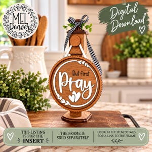 May include: A circular wooden sign insert featuring the text But first Pray in white lettering with two small hearts. The sign is accented with a black and white gingham ribbon bow at the top and a white leaf wreath design.