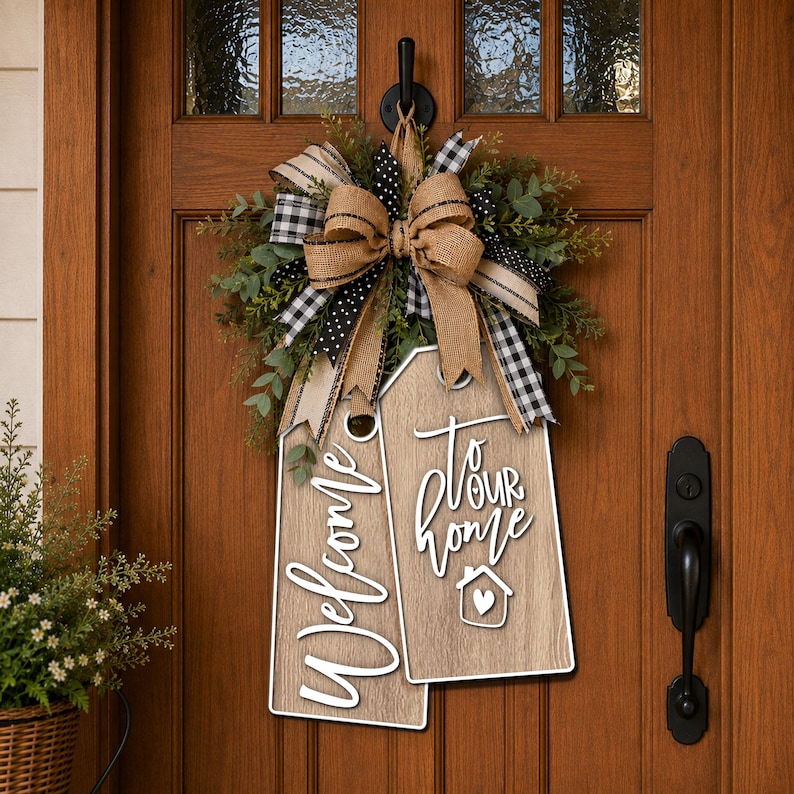 May include: A decorative door hanging featuring two light brown wood-grain tags with white text reading Welcome and to our home with a small house icon. A large bow made of burlap, black and white buffalo check, and polka dot ribbon sits above.