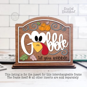 May include: A wooden sign insert featuring the text Gobble 'til you wobble with a turkey face integrated into the word Gobble. The design includes orange pumpkins, green and pink leaves, and blue swirls on a dark wood background with a white border.