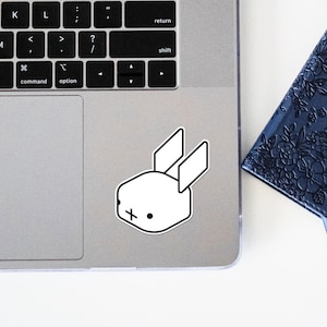 Peut inclure: Un autocollant blanc représentant un lapin de dessin animé avec des contours noirs sur un ordinateur portable argenté.