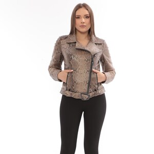 May include: A tan and brown snakeskin-patterned leather jacket with a black zipper and belt. The jacket has a classic biker style with a notched collar and pockets. The model is wearing black leggings and black high heels.