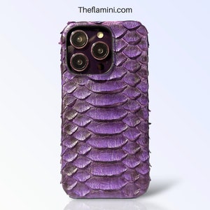Może przedstawiać: Fioletowe etui na telefon z teksturowanym wzorem przypominającym łuski. Etui ma wycięcie na aparat z trzema obiektywami i lampą błyskową. Theflamini.com jest wydrukowane u góry. Dla smartfona.