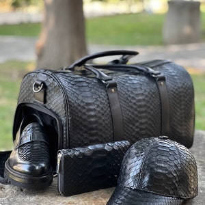 Pode incluir: Um conjunto de acess&oacute;rios em couro preto com textura de pele de cobra. Inclui uma mala de viagem, mocassins, uma carteira e um bon&eacute; de beisebol. A mala tem uma al&ccedil;a superior e uma al&ccedil;a de ombro.